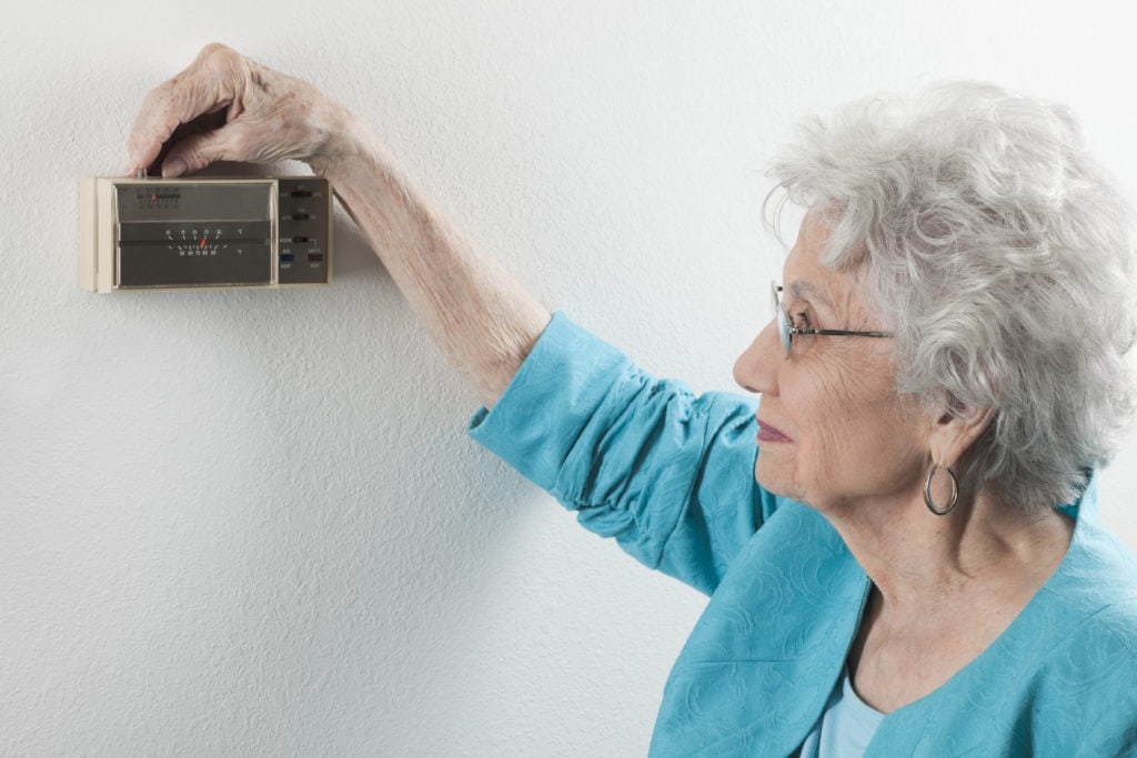 senior woman adjusting home thermostat