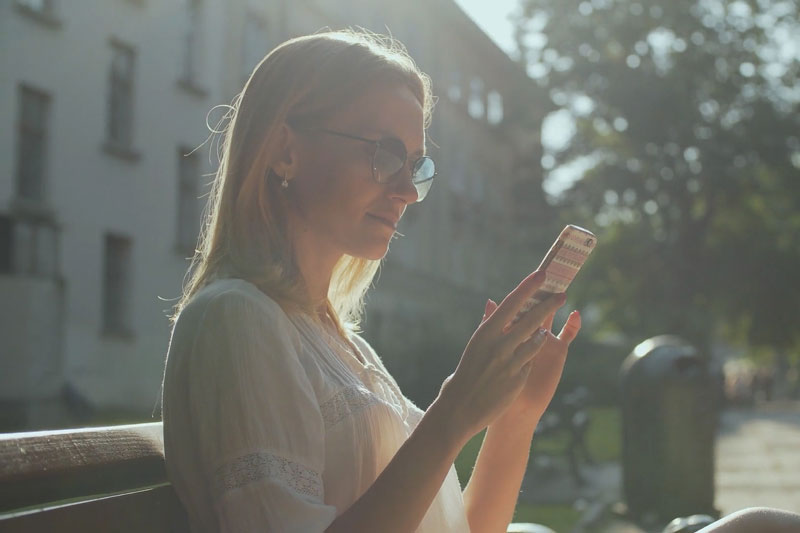 woman controlling her Wi-Fi Thermostat from the park