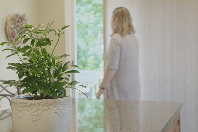 A woman standing in her home looking out of the blinds.