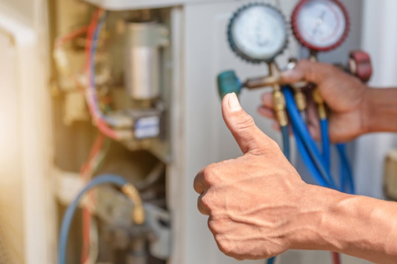 Spring AC Maintenance Tips. Photo of a repairman inspecting an air conditioner and giving a thumbs up.